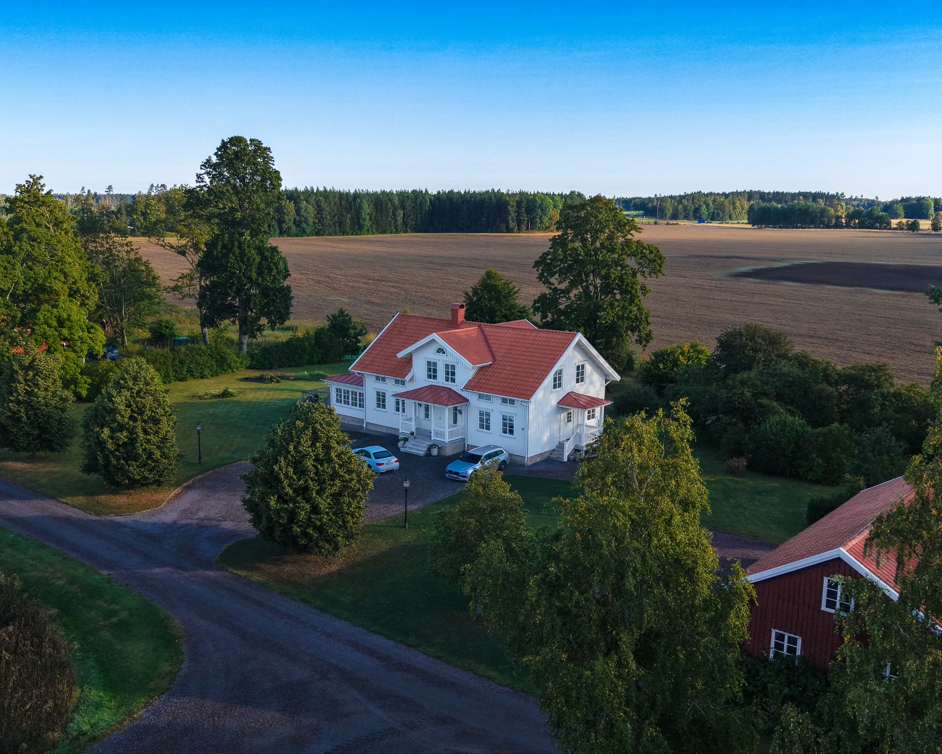 Drönarbild av ett vitt hus med rött tak omgivet av åkrar och träd