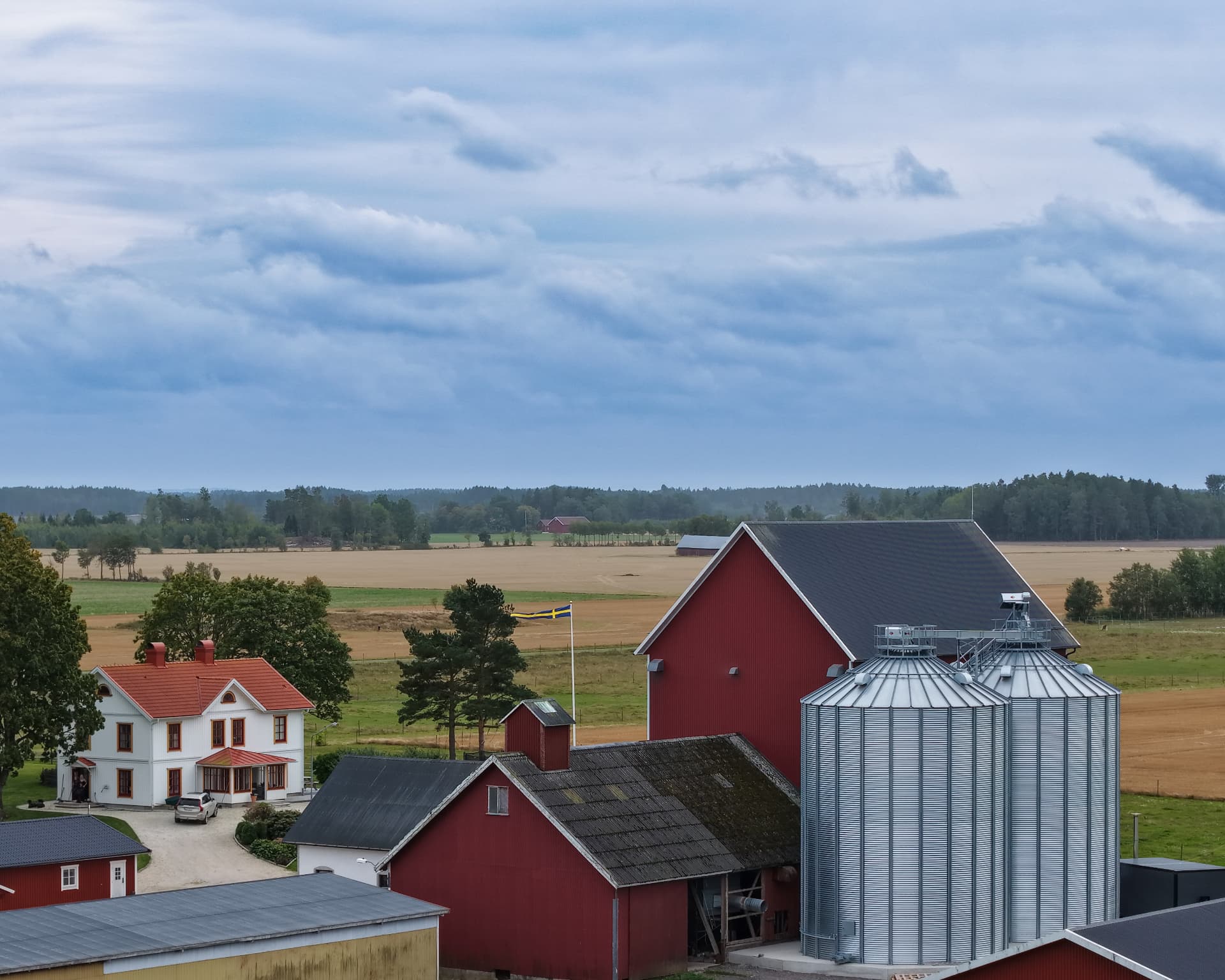 Gård med röd lada, silor och svenskt hus med flaggstång