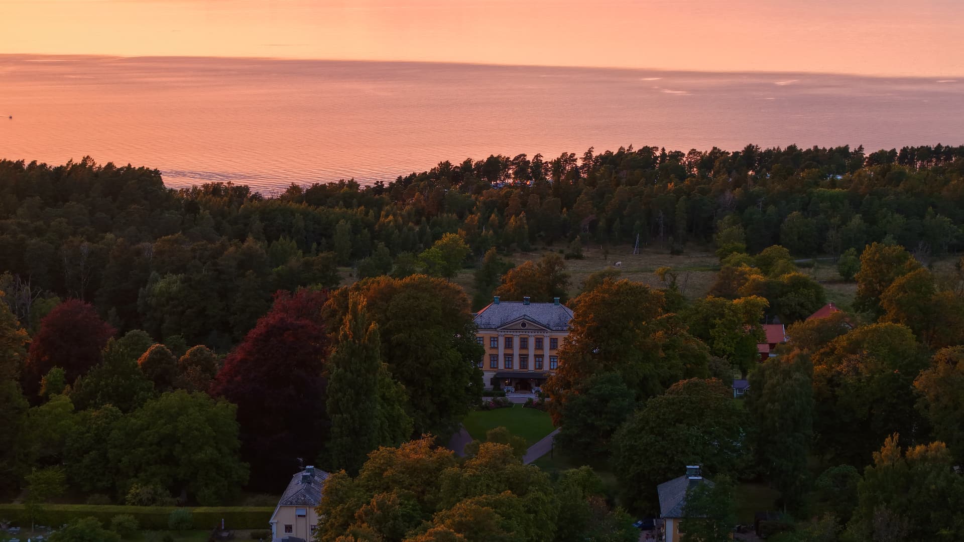 Herrgård bland träd med Vänern i kvällsljus bakom